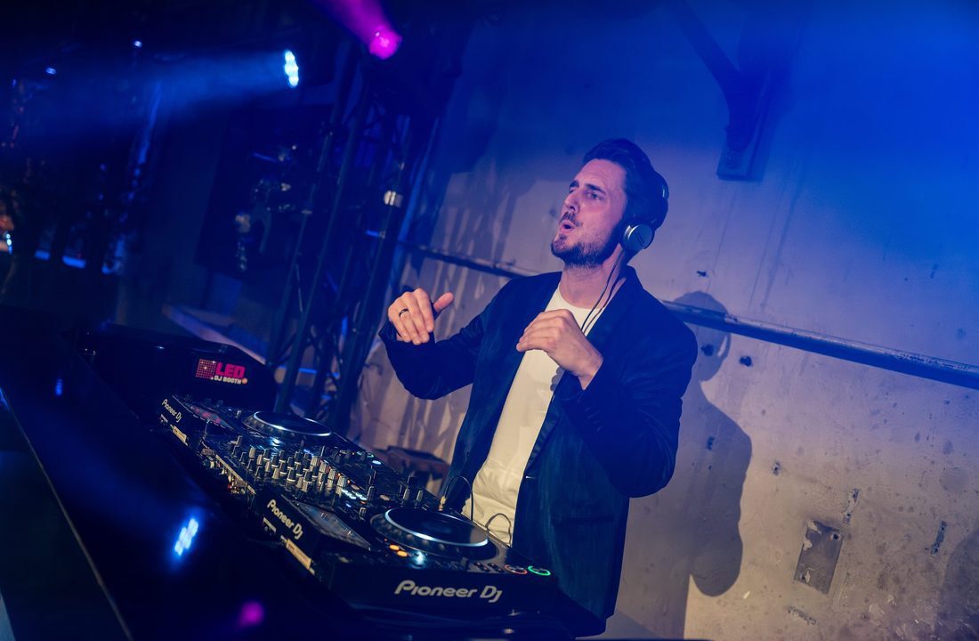 DJ achter professionele apparatuur in blauw en paars podiumlicht