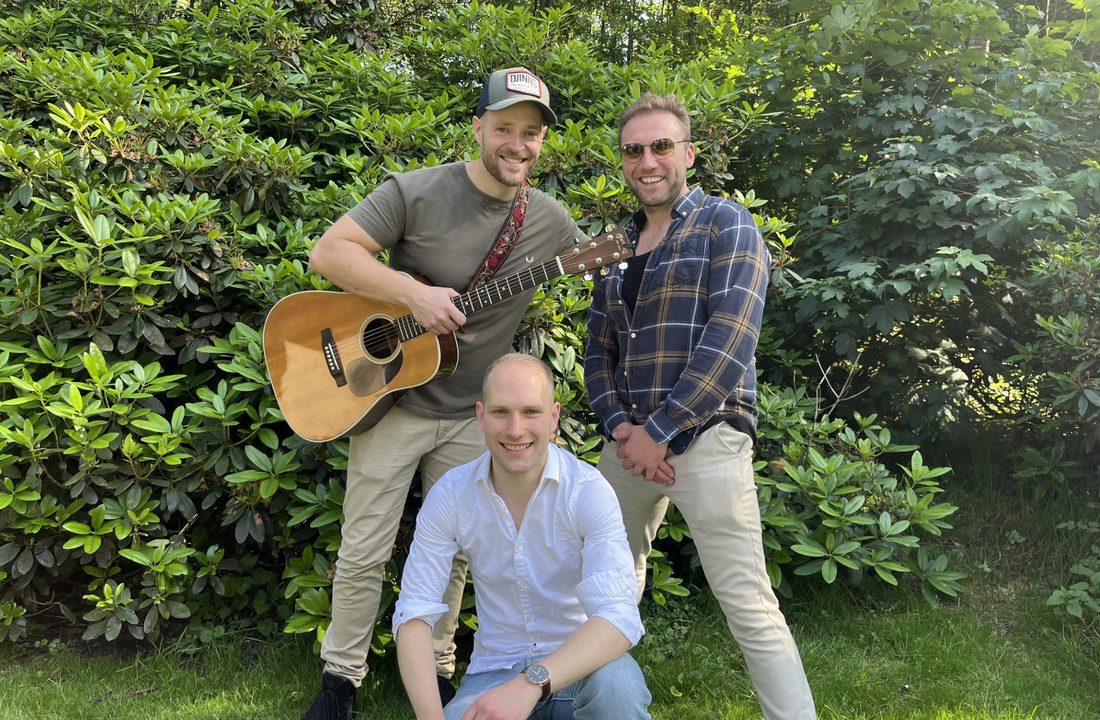 Drie muzikanten poseren buiten met een akoestische gitaar