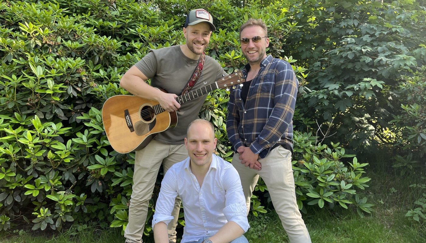 Drie muzikanten poseren buiten met een akoestische gitaar